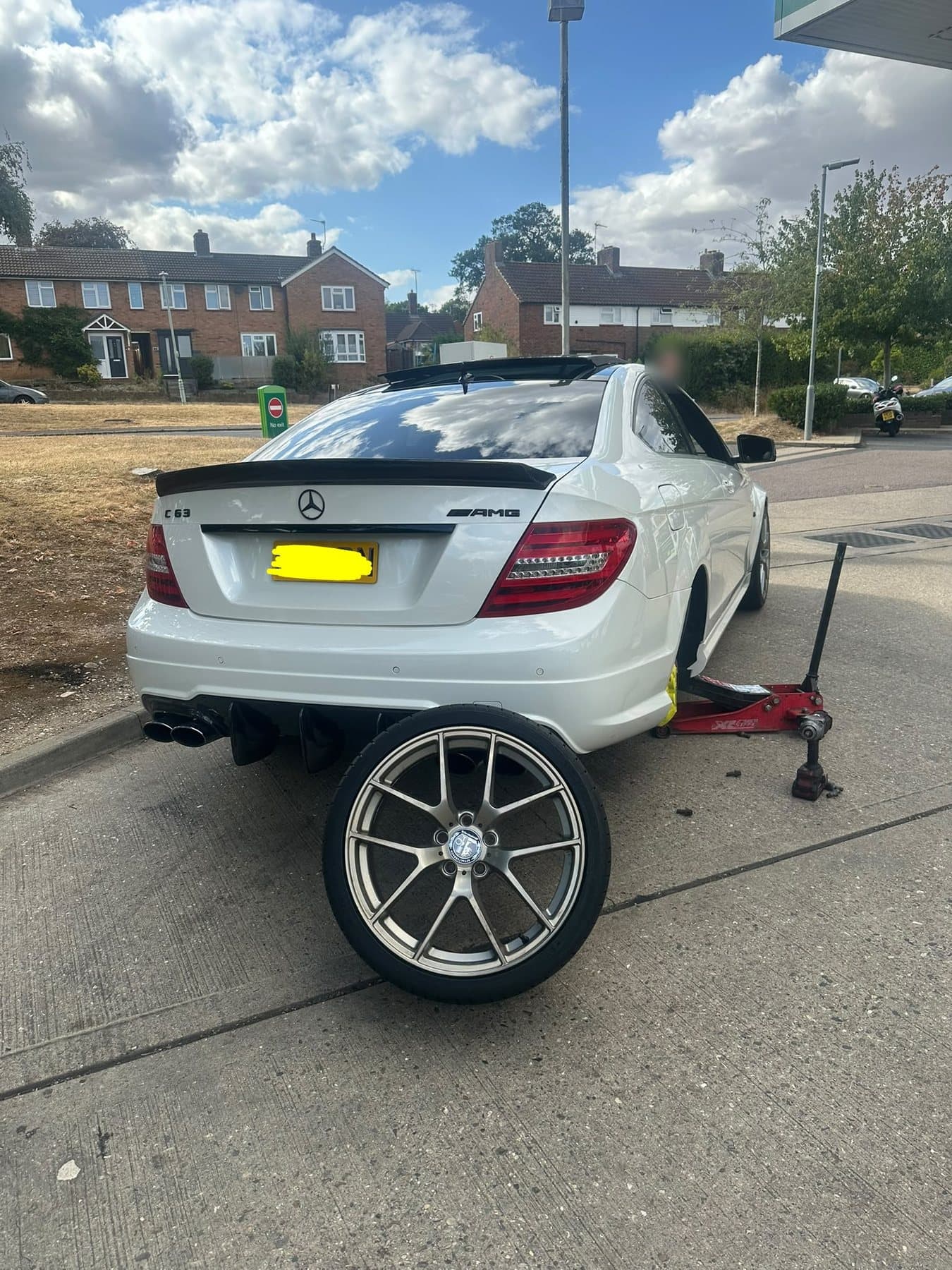 A white Mercedes coupé on a trolley jack with one rear wheel removed and standing upright on the forecourt